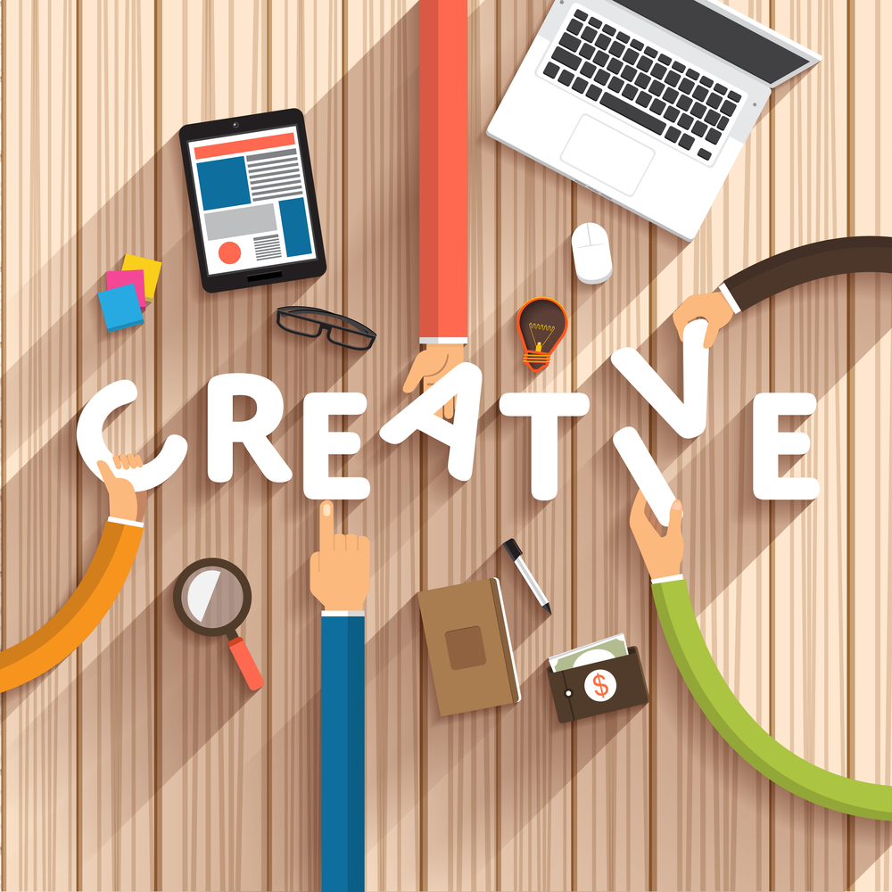 Graphic with the words creative in white and long arms reaching to the middle of the table surrounded by a laptop, tablet, notebook, wallet, sticky notes, magnifying glass and light bulb.